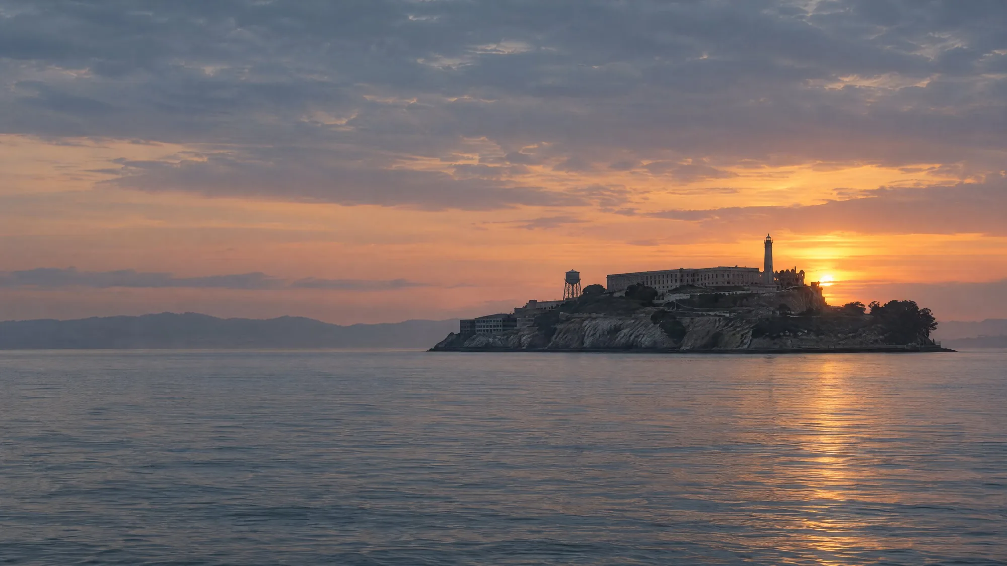 Alcatraz Island at dusk, the sun low and soft behind it over a calm bay